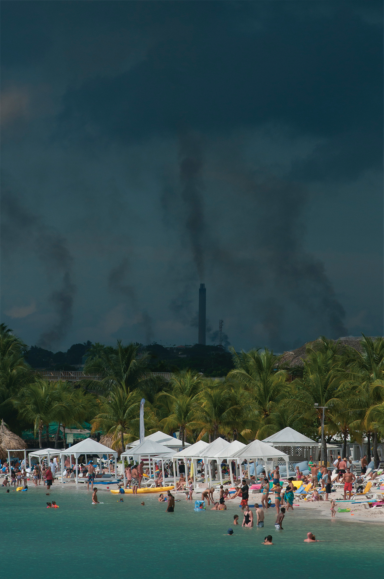 Toeristen op Curaçao, met op de achtergrond de ISLA-olieraffinaderij.