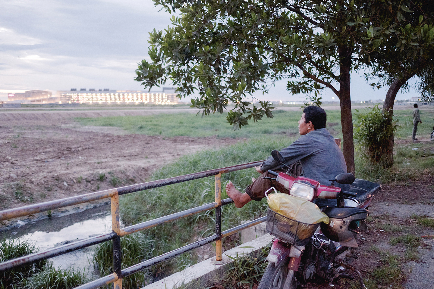 Vanaf zijn motorfiets staart een man naar het lege stuk land bij Phnom Penh waar binnenkort een winkelcentrum verrijst.