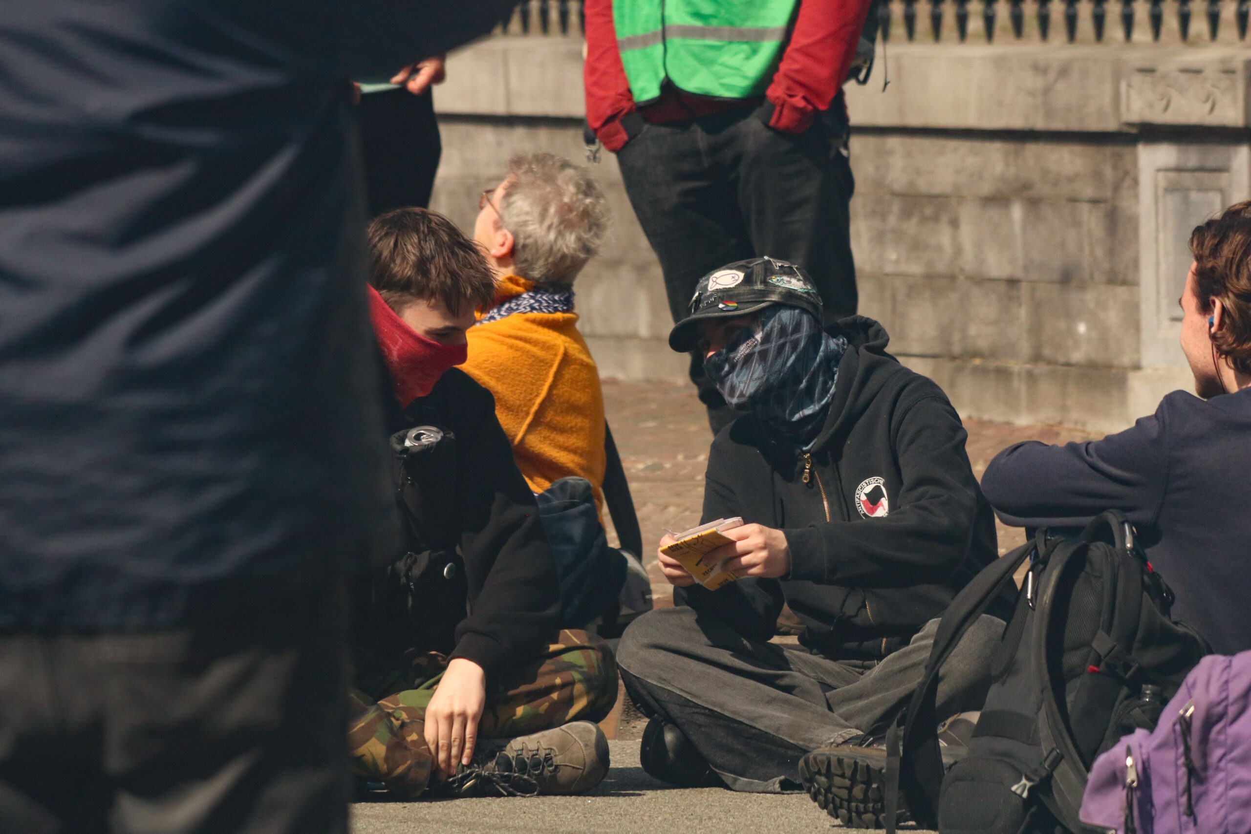Een groepje demonstranten is gaan zitten op het asfalt van de N205. Om niet het risico te lopen herkenbaar in de politiedatabase terecht te komen, hebben ze hun gezicht bedekt.
