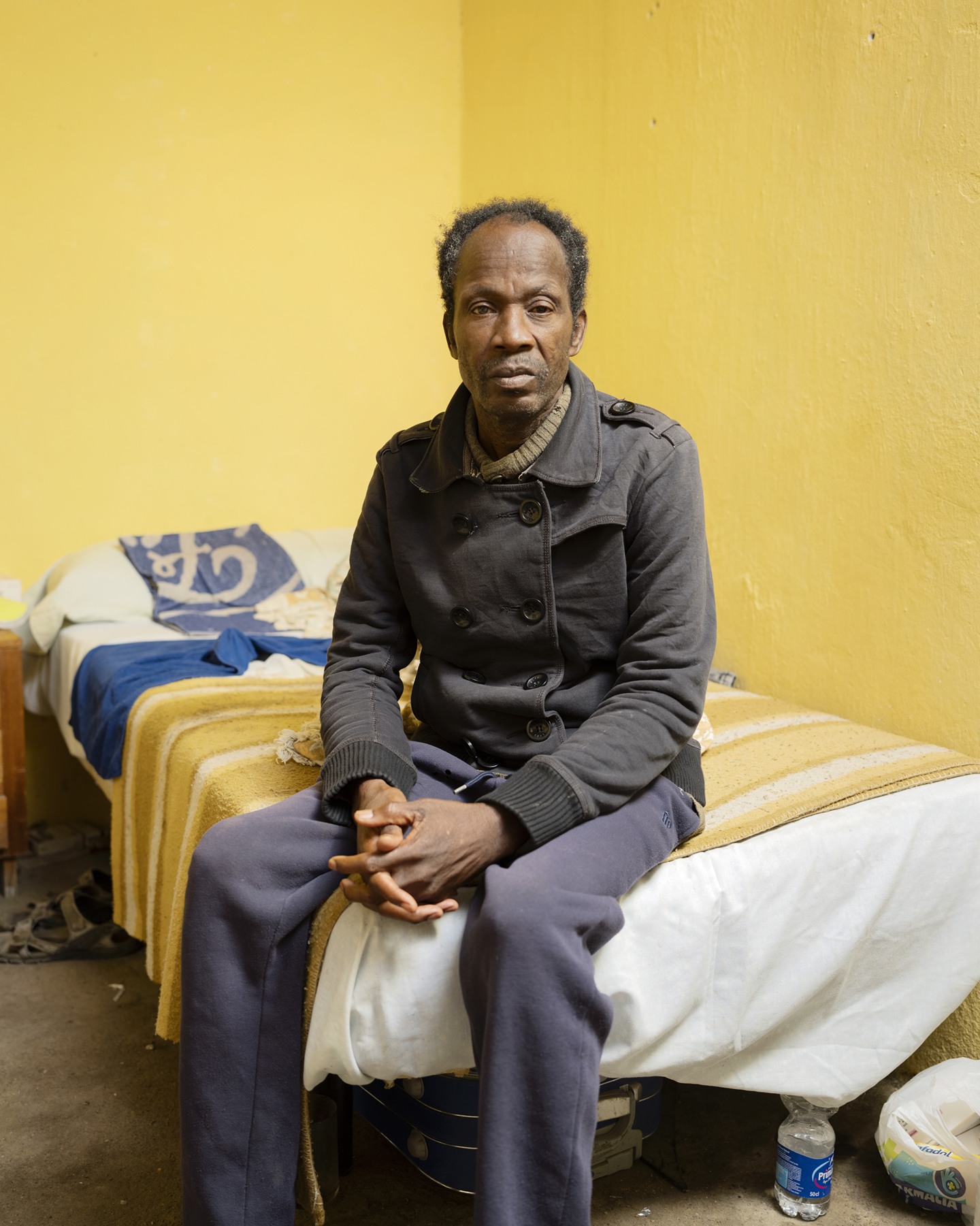 Een plukker zit op een bed, in een van de weinige stenen huisjes in de sloppenwijk.